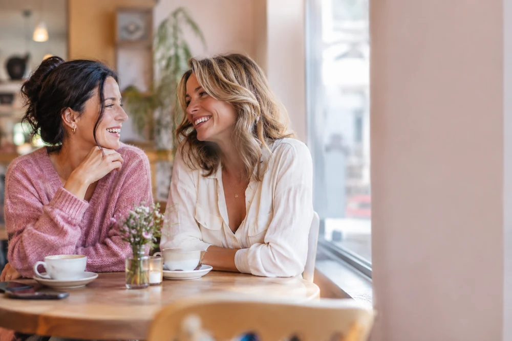 Reconnaître son âme sœur : deux amies rient ensemble à une table de café, complicité sincère