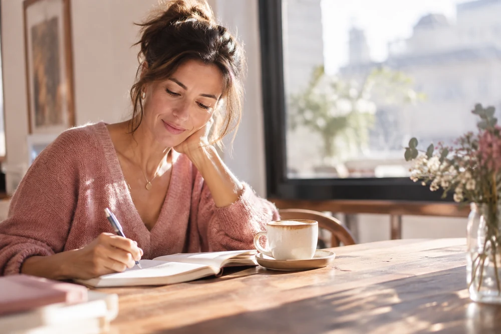 Ce qui est possible en 24h : une femme écrit un plan dans un carnet au soleil, tasse de café