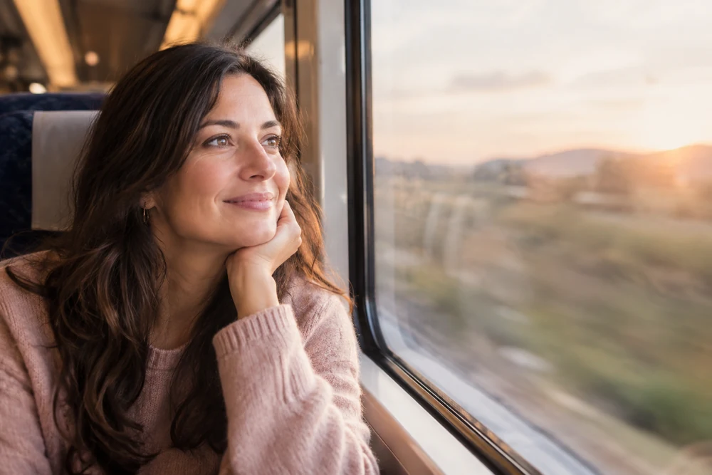 Ex âme sœur : une femme sourit en regardant par la fenêtre d'un train, paysage flou, lumière dorée