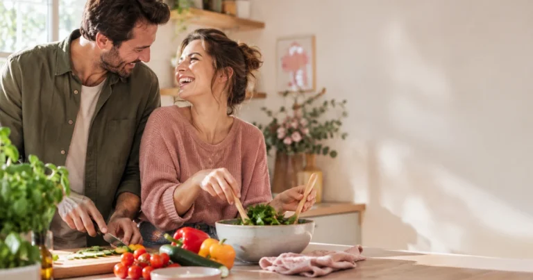 Lien durable en couple : un couple rit ensemble en préparant un repas dans une cuisine lumineuse, complicité naturelle
