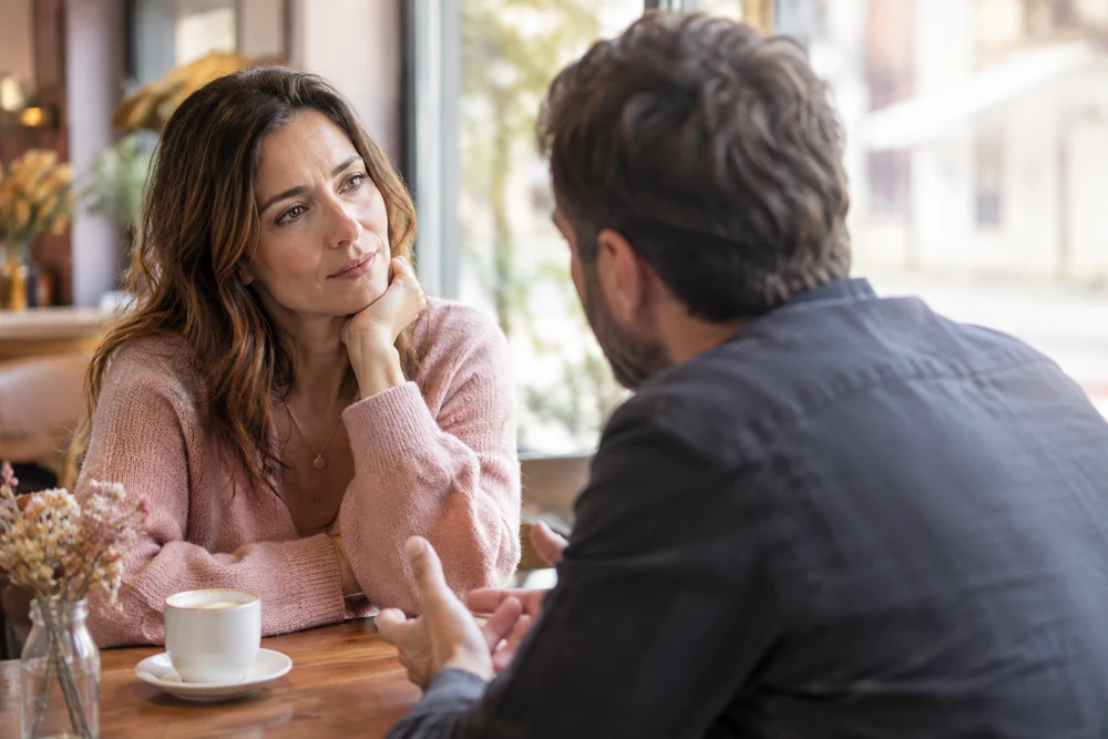 Regret sincère d'un homme : une femme écoute calmement un homme qui s'explique, assis face à face dans un café